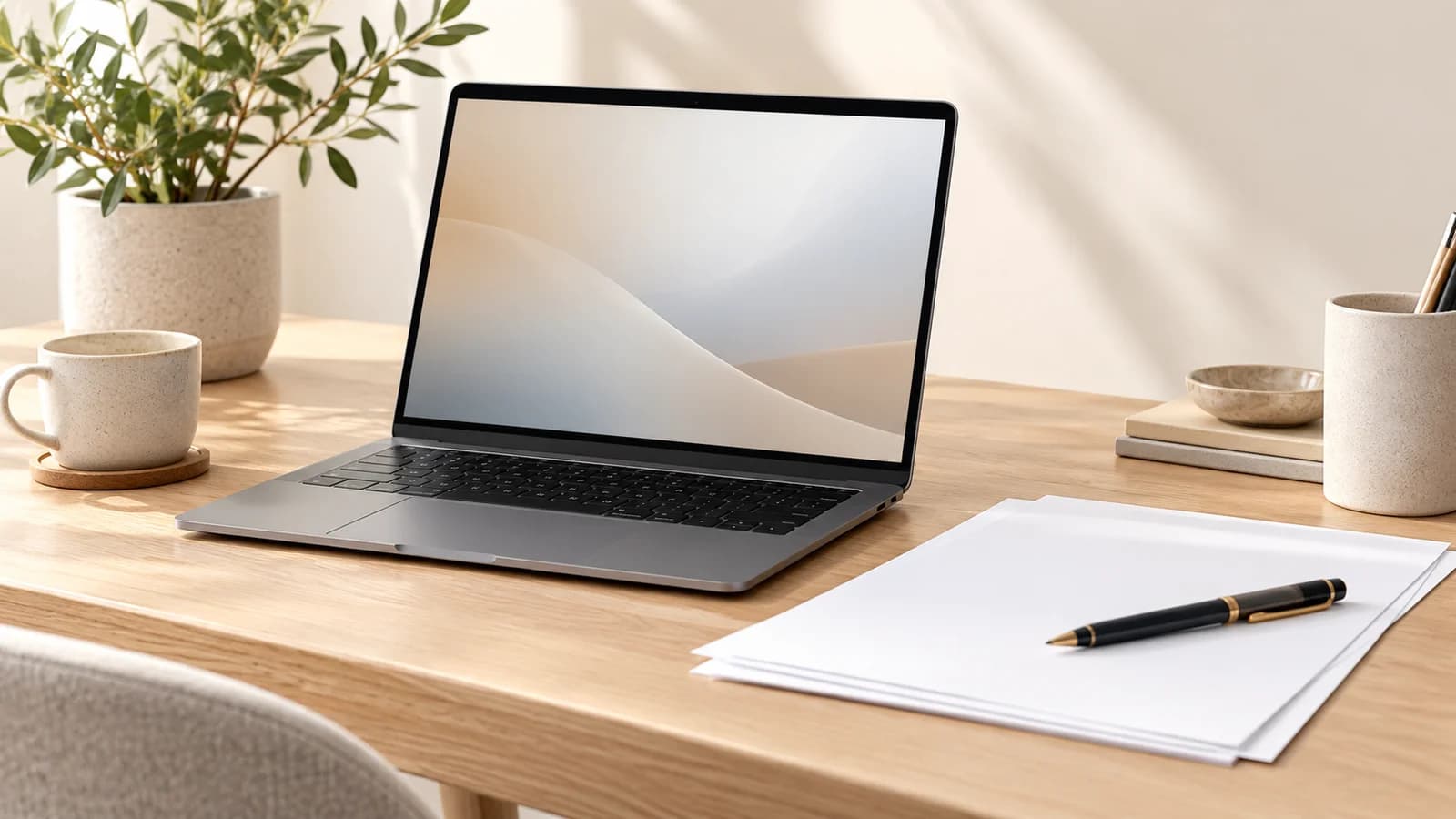An open laptop, blank documents, and a pen on a bright neutral desk